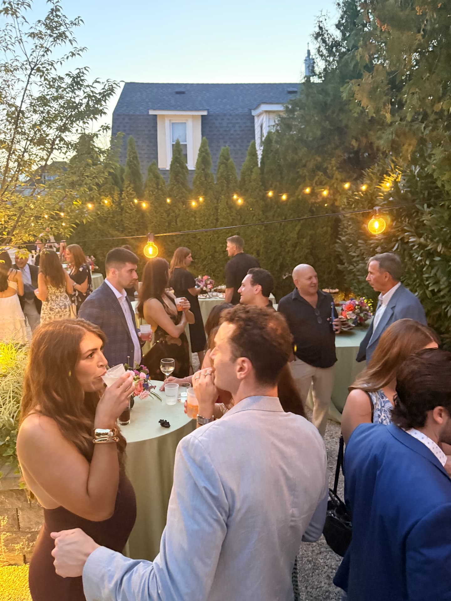 Guests socializing with drinks under string lights at a wedding welcome party
